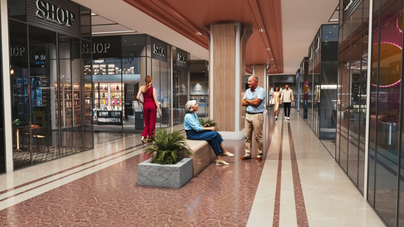 Spacious modern shopping mall corridor with retail shops on both sides. People walking, browsing, and sitting on benches surrounded by indoor plants. Bright, contemporary interior design with polished floors and stylish lighting, creating a welcoming shopping experience.